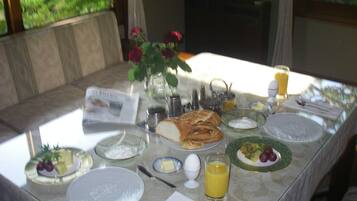Mesa de café da manhã posta com pratos, pão, ovos, frutas e um copo de suco de laranja.