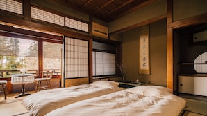A traditional Japanese room with tatami flooring, two beds, a small table with chairs, and sliding doors.