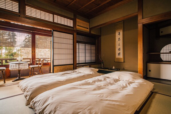 Une pièce de style japonais traditionnel, avec un sol recouvert de tatamis, deux lits, une petite table et des chaises, ainsi que des portes coulissantes.