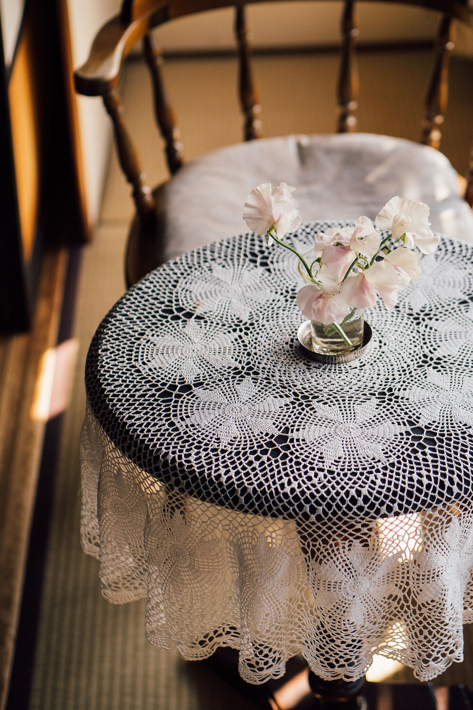 A round table with a lace tablecloth and a vase with flowers.