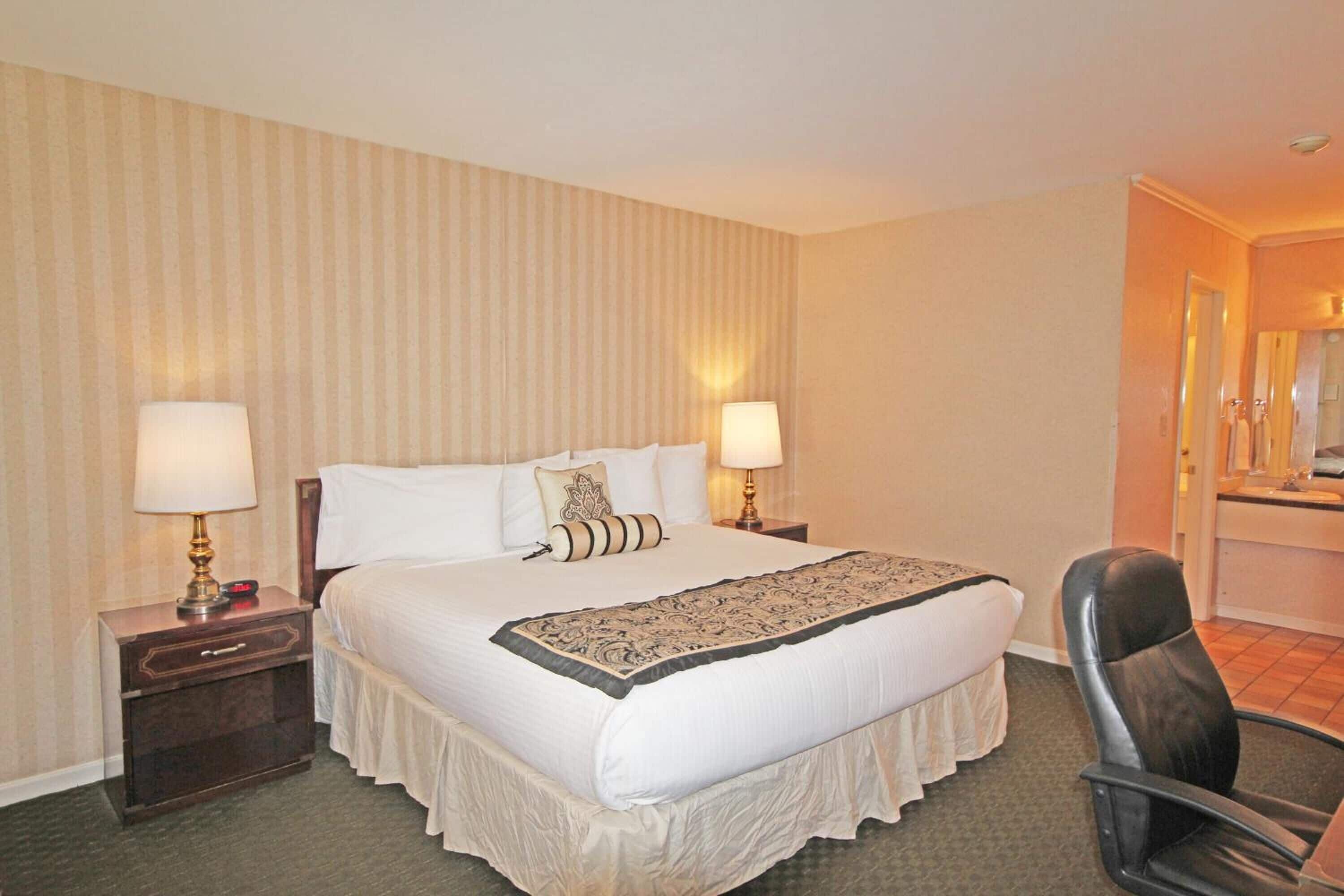 A hotel room with a large bed, two bedside tables with lamps, a chair, and a mirror.