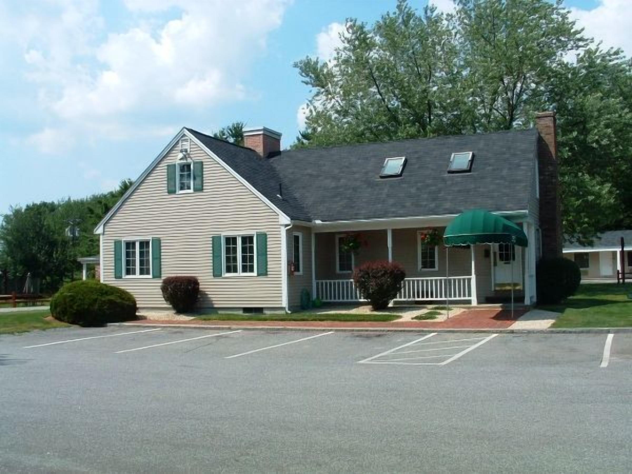 A two-story building with a gabled roof, a covered porch, and a parking lot in front.
