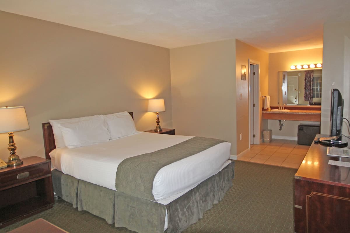 A hotel room with a bed, bedside lamps, a desk with a computer, a mirror, and a small kitchenette.