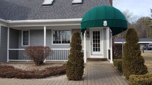 Een huis met een overdekte veranda, een kleine tuin met struiken en een auto op de oprit.