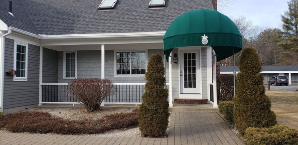 A house with a covered porch, a small garden with shrubs, and a car parked in the driveway.