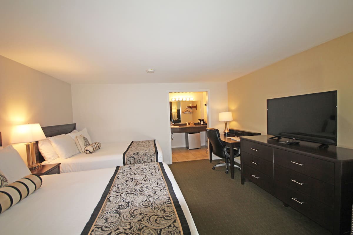 A hotel room with two beds, a desk, a television, and a bathroom visible through an open door.