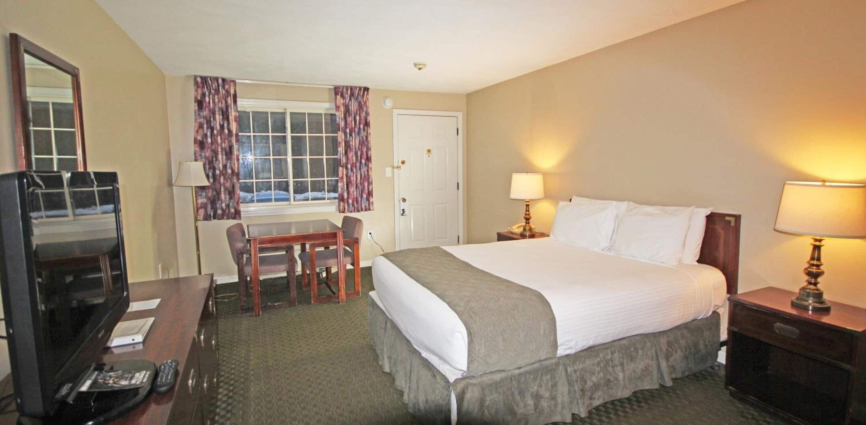 Een hotelkamer met een bed, een bureau, een stoel, een televisie en een raam met gordijnen.