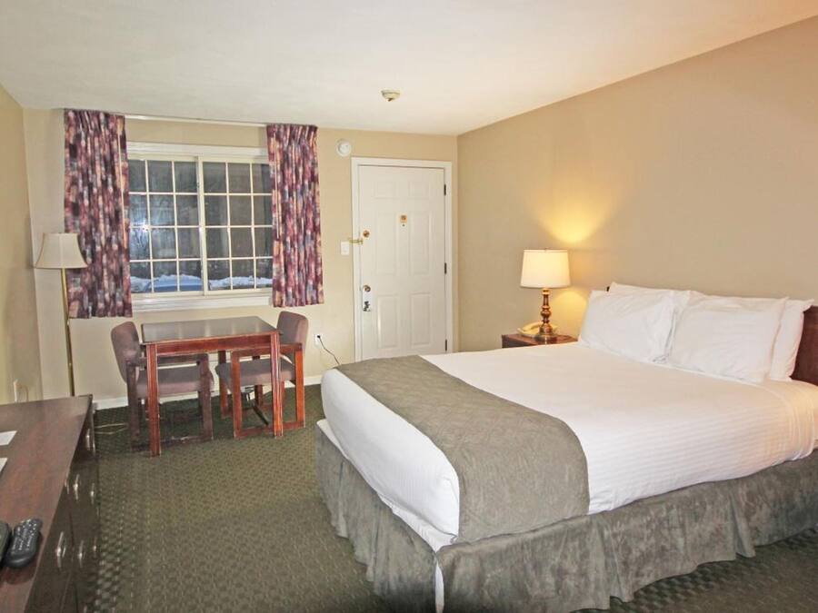 A hotel room with a bed, a desk, a chair, a television, and a window with curtains.