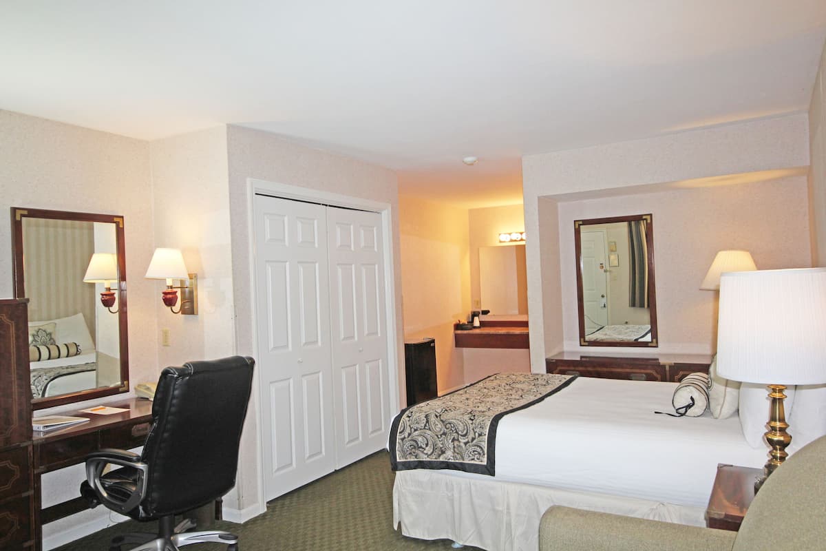 A hotel room with a bed, desk, chair, and two mirrors.