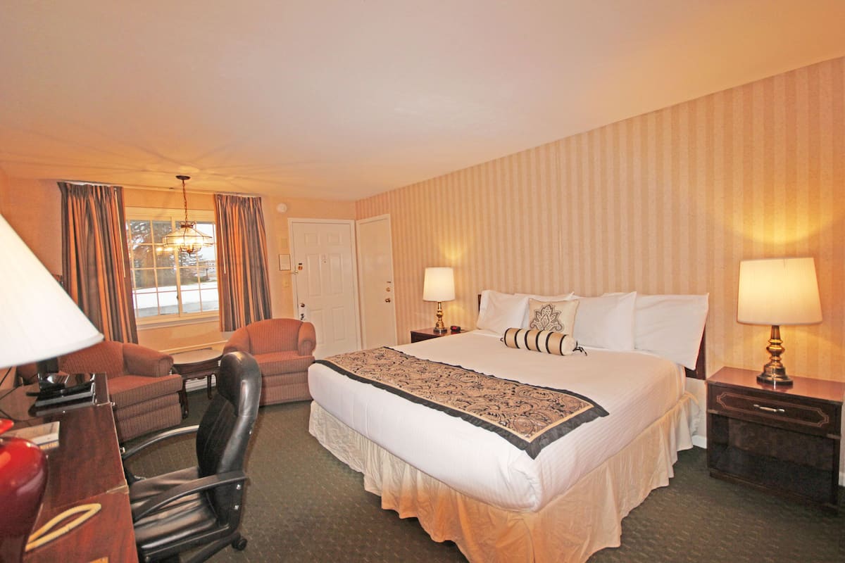 A hotel room with a large bed, two bedside lamps, a desk with a lamp, a chair, and a window with curtains.