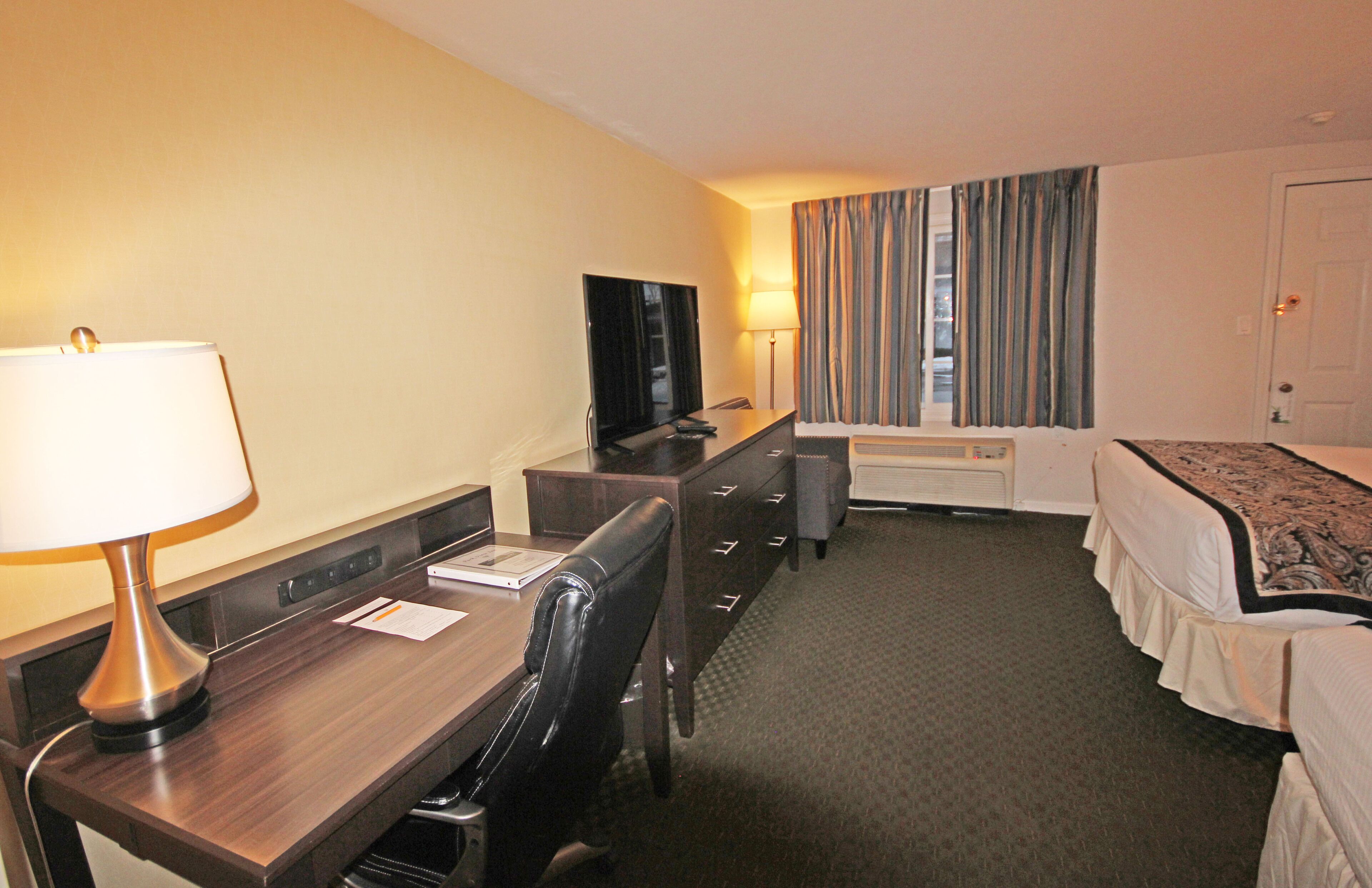 Una habitación de hotel con escritorio, silla, televisor, cama y cortinas.