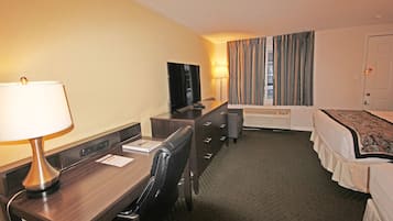 Ein Hotelzimmer mit Schreibtisch, Stuhl, Fernseher, Bett und Vorhängen.