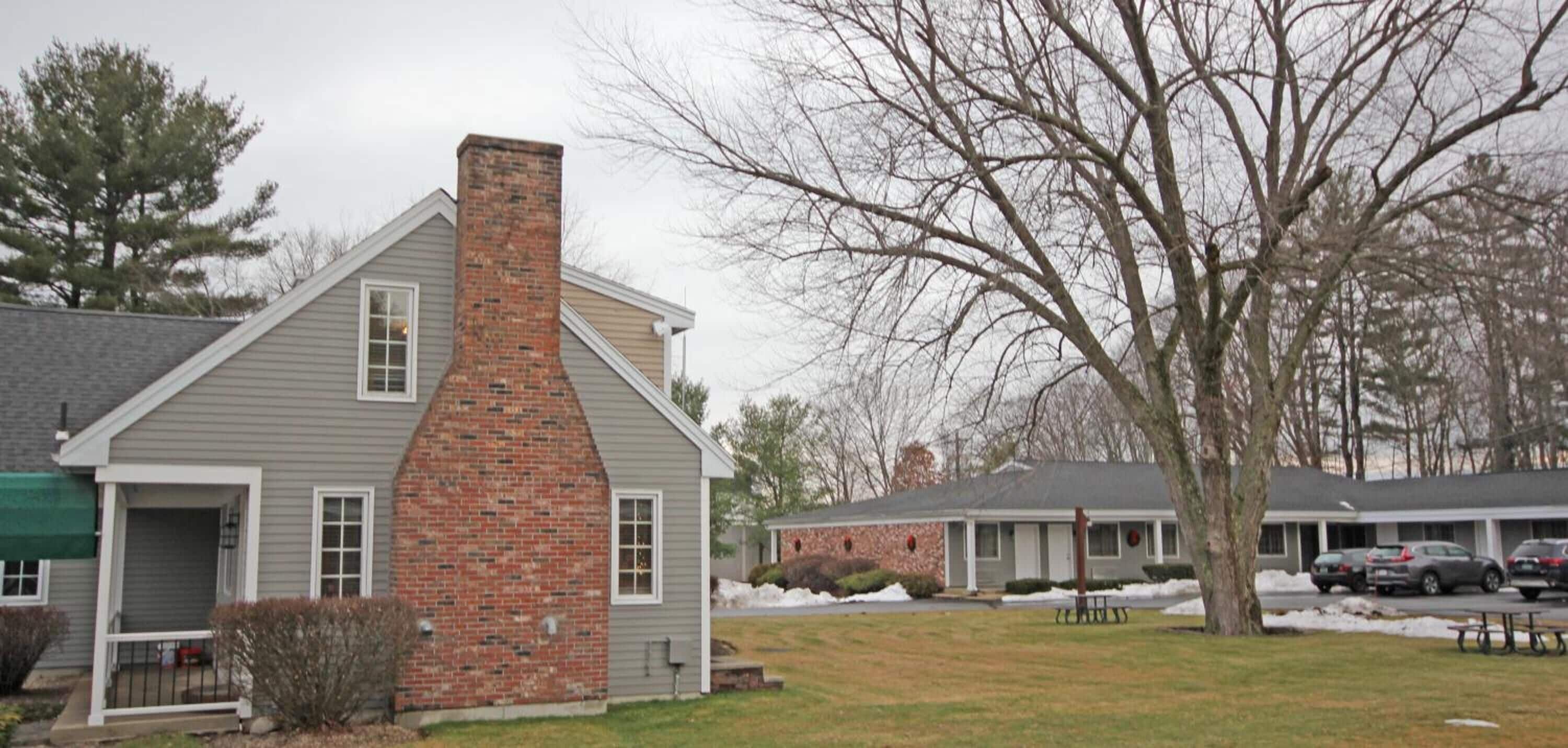 A two-story building with a brick chimney, a covered porch, and a parking area with cars.