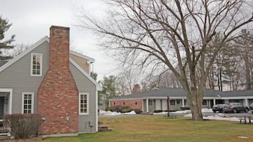 A two-story building with a brick chimney, a covered porch, and a parking area with cars.