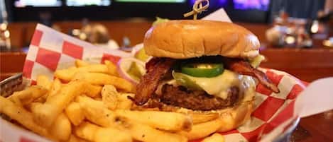Ein Burger mit Speck, Käse und Jalapeños auf einem Brötchen, dazu Pommes.