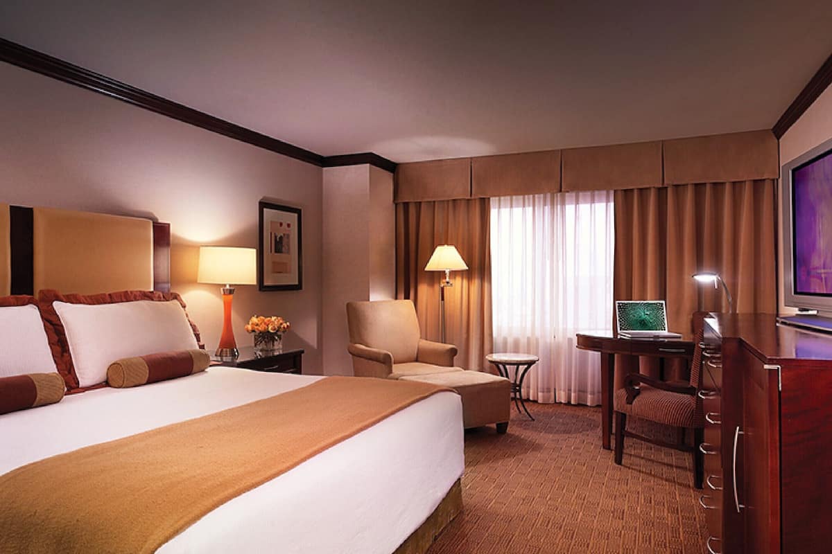 A hotel room with a large bed, a desk with a laptop, a chair, and a television.