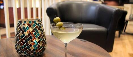A cocktail glass with olives on a wooden table, a mosaic vase, and a black leather couch in the background.
