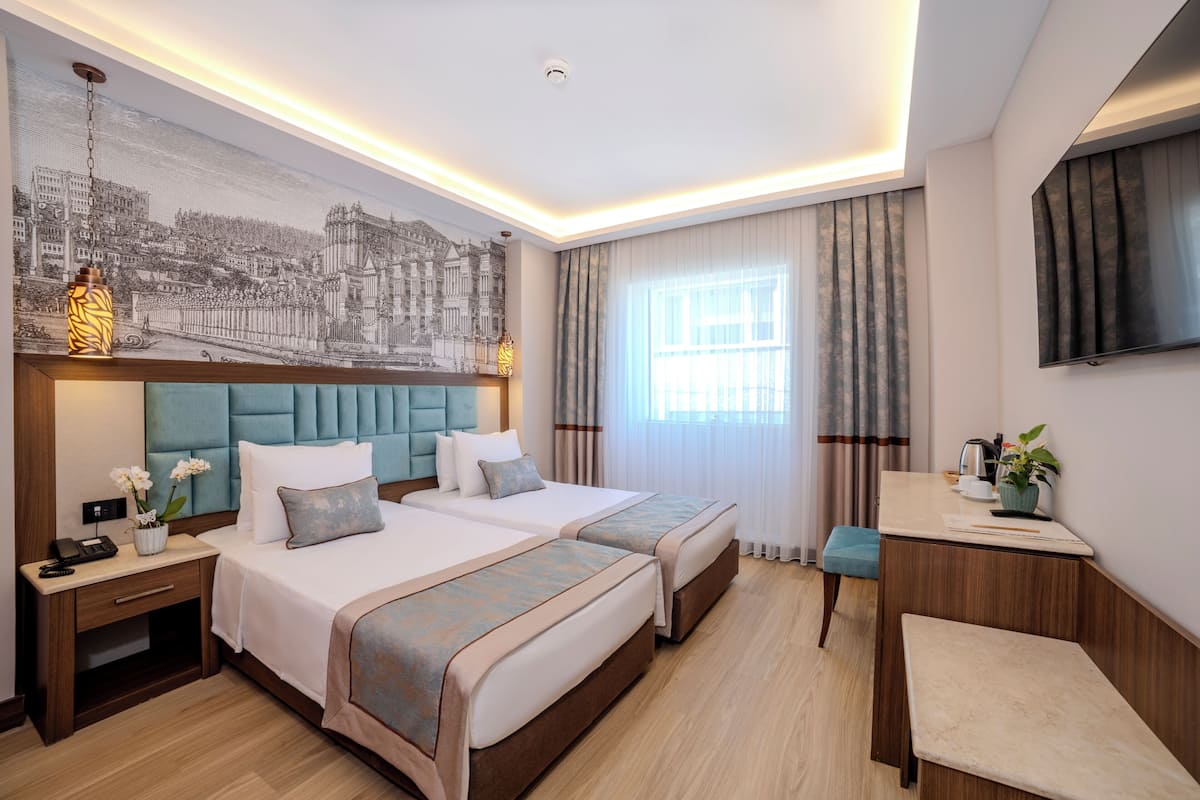 A hotel room with two beds, a desk, a chair, a TV, and a large window with curtains.