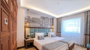 A hotel room with two beds, a large wall mural, a wooden wardrobe, and a nightstand with a lamp. - Grand Hilarium Hotel (Istanbul)