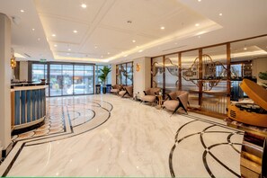 A spacious lobby with a marble floor, seating area, reception desk, and a staircase with a decorative railing. - Grand Hilarium Hotel (Istanbul)
