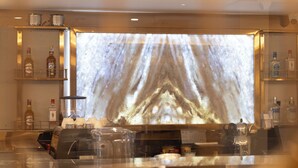 A bar area with a large screen displaying a mountain image, shelves with liquor bottles, and bar equipment. - Grand Hilarium Hotel (Istanbul)