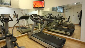 Een sportschool met loopbanden, elliptische trainers en een televisiescherm.
