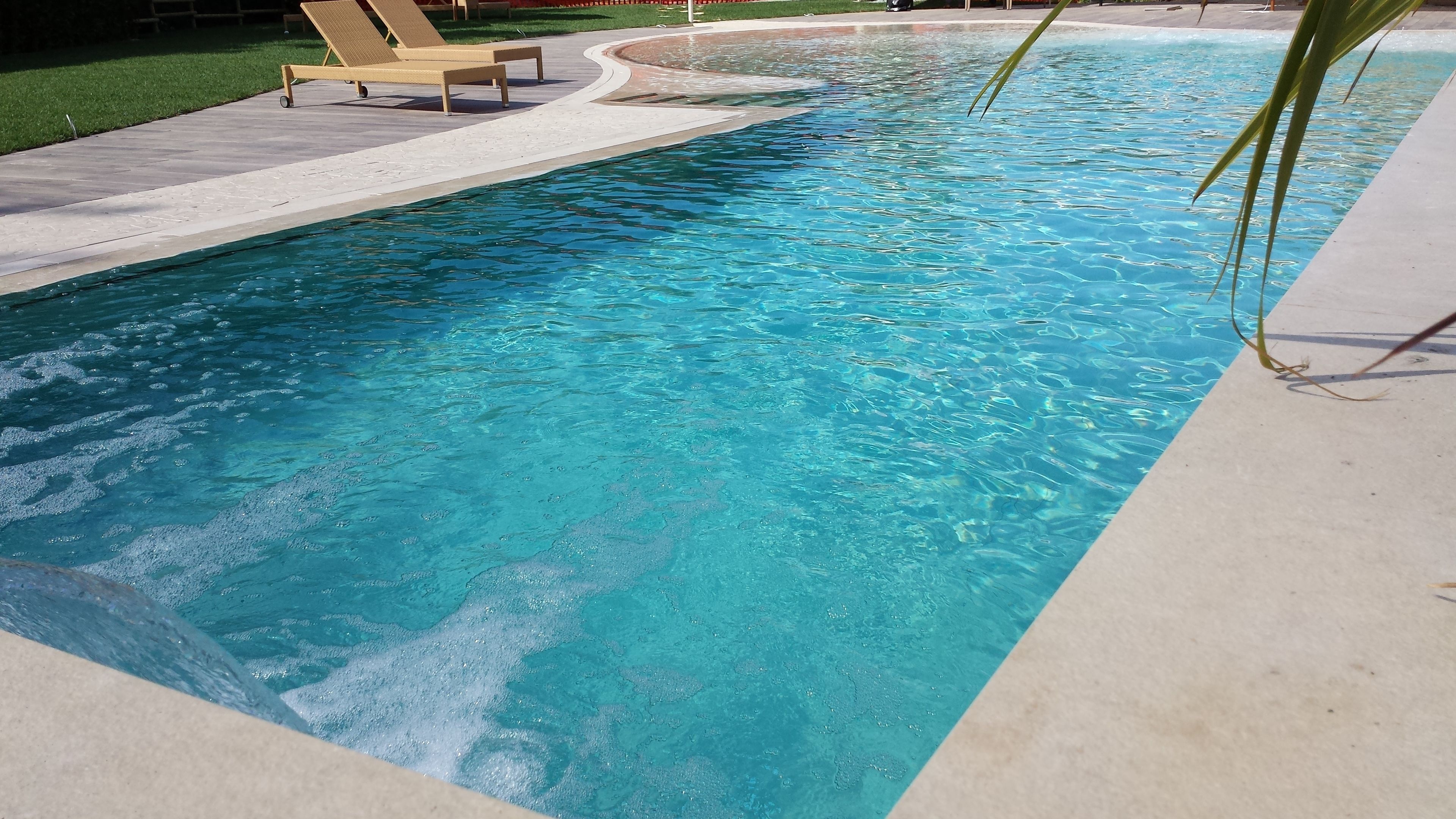 A rectangular swimming pool with clear blue water, surrounded by a concrete deck and a grassy area with lounge chairs.