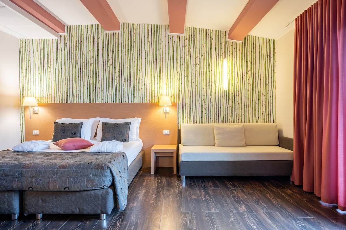 Une chambre d’hôtel avec un lit, un canapé, une table de chevet et un mur à rayures verticales.