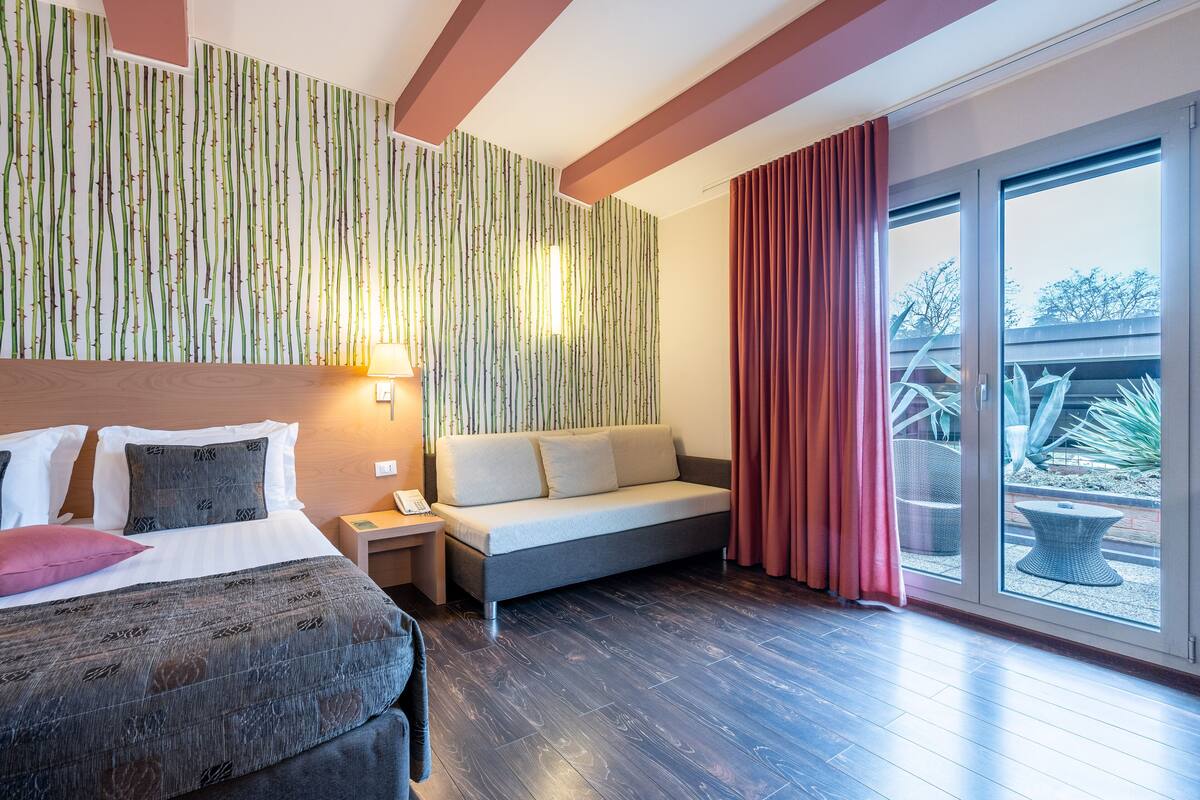 Une chambre d’hôtel comprenant un lit, un canapé, une table de chevet et une grande fenêtre donnant sur l’extérieur.
