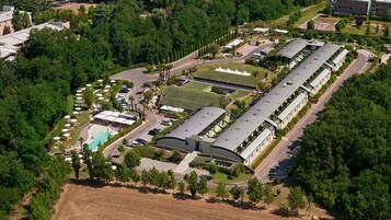 An aerial view of a hotel with multiple buildings, a swimming pool, and surrounding greenery.