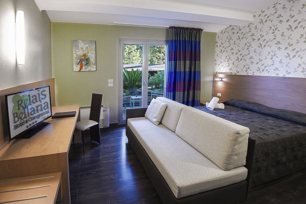 Une chambre d’hôtel équipée d’un canapé, d’un lit, d’une télévision, d’un bureau et offrant une vue sur l’extérieur.
