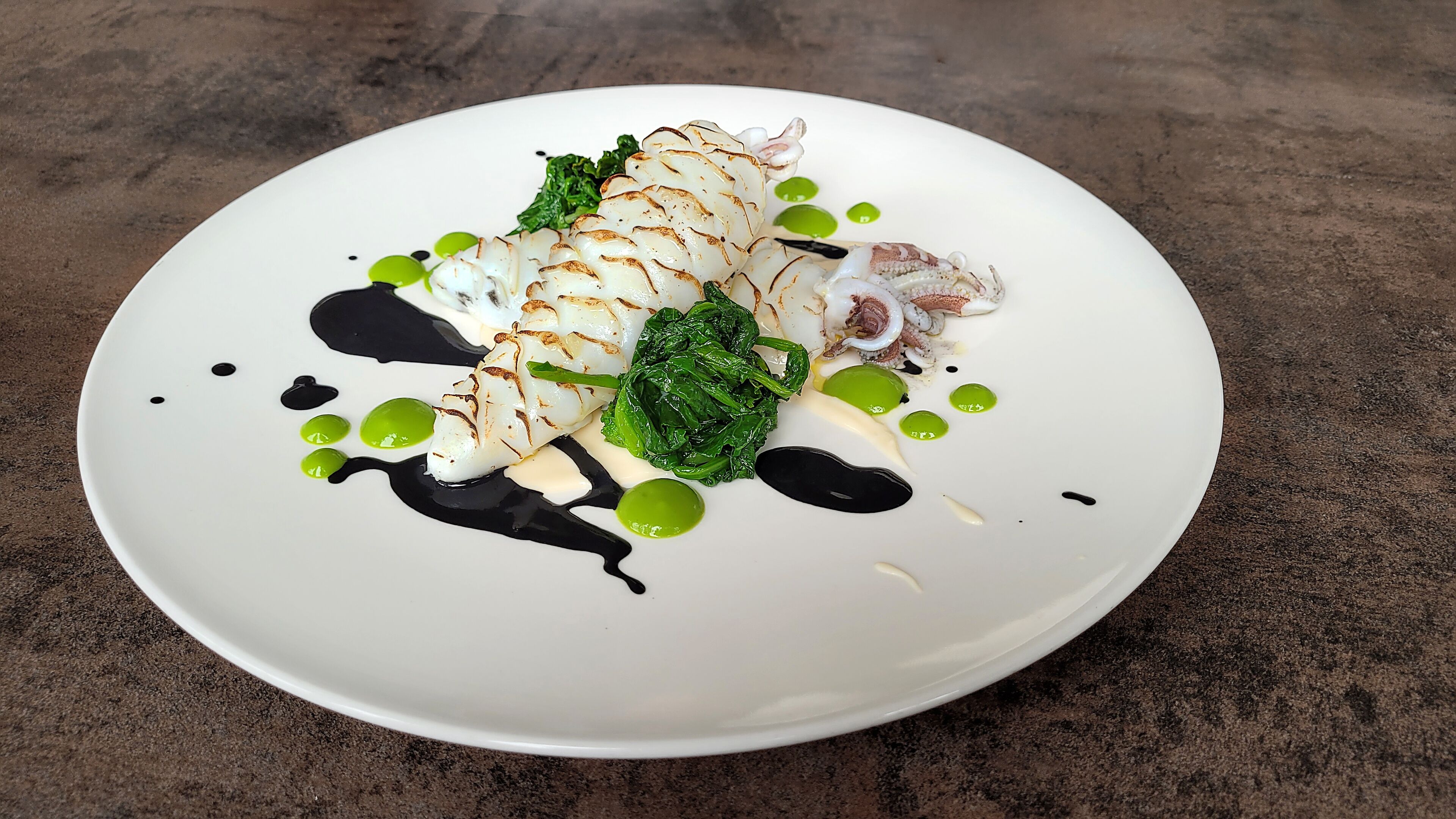 Un plato blanco con un guiso de mariscos, salsa verde y salsa negra.