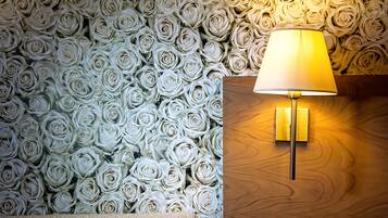 Eine Wand mit geprägter Tapete mit weißen Rosen und einer Wandleuchte auf einer Holzbodenfläche.