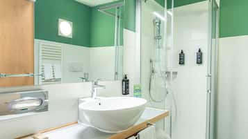 Un bagno moderno con un ampio lavandino bianco, una doccia vetrata e pareti verdi.