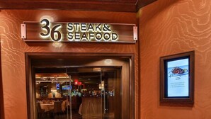 Een hotelentree met een bord voor kamer 36 Steak & Seafood, een glazen toegangsdeur en een vloerkleed met een geometrisch patroon.