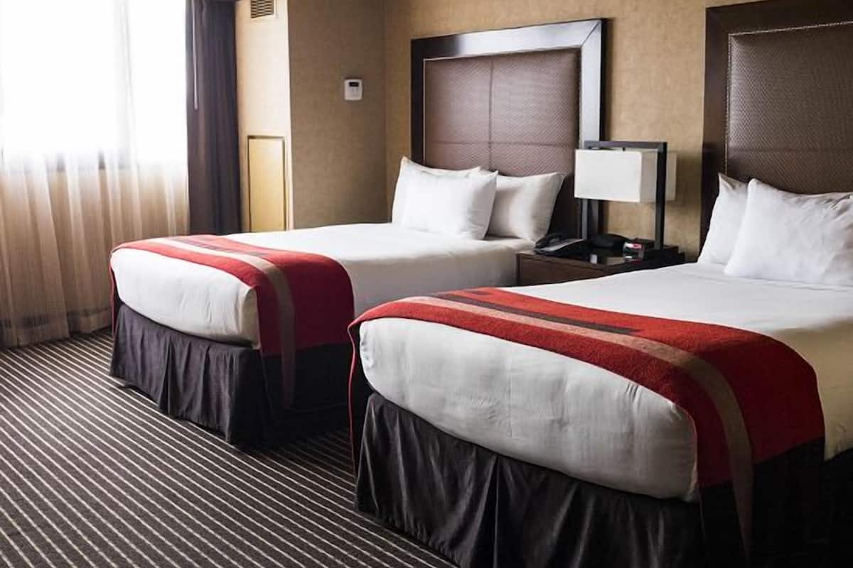 Une chambre d’hôtel avec deux lits, une table de chevet avec une lampe et une fenêtre avec des rideaux.