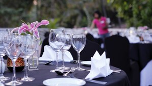 Una mesa dispuesta para una comida, con vasos transparentes, un arreglo floral y un mantel negro.