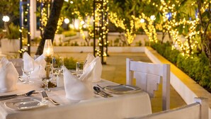 An outdoor dining area with tables set for a meal, string lights, and a view of greenery.
