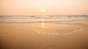 A beach with waves, a clear sky, and the sun setting or rising.