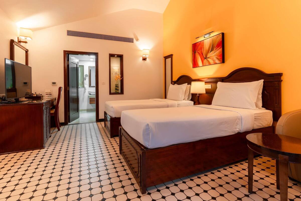 Ein Hotelzimmer mit zwei Betten, einem Schreibtisch mit Computer, einem Spiegel und einem Bild an der Wand.