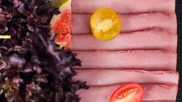 Primer plano de rebanadas de jamón con rodajas de tomate sobre un fondo oscuro.