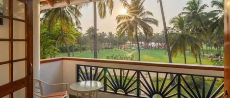 A balcony with a view of a lawn and palm trees, a table, and two chairs.