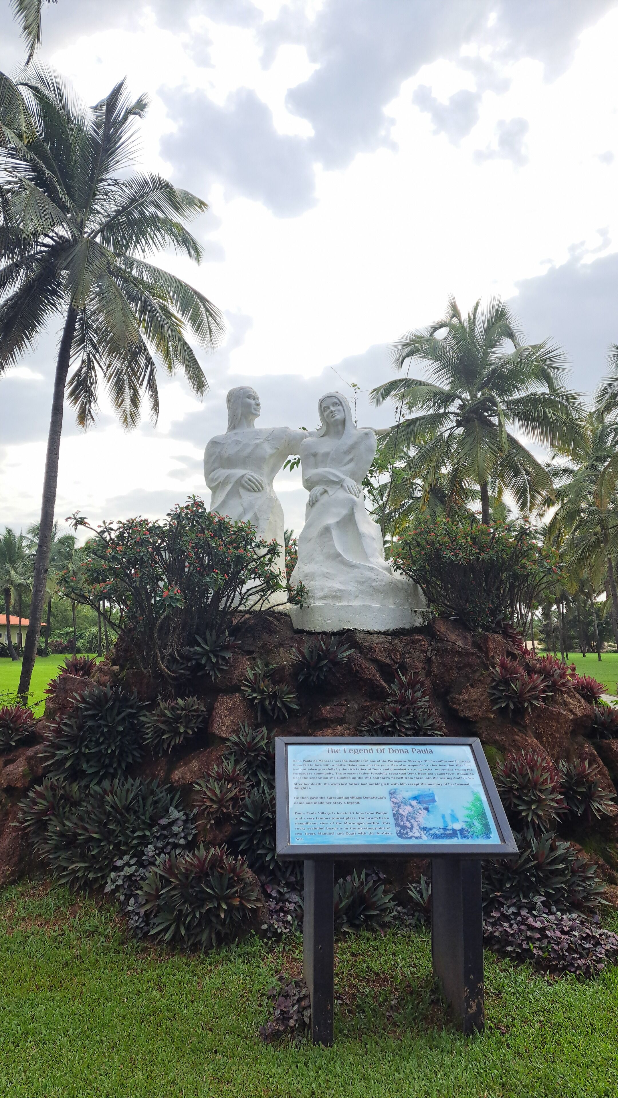 Una estatua de dos figuras con un cartel informativo al frente.