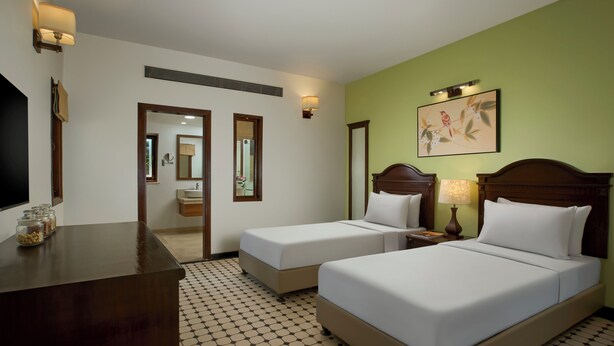 A hotel room with two single beds, a desk, a mirror, and a painting on the wall. - Novotel Goa Dona Sylvia Resort (Cavelossim)