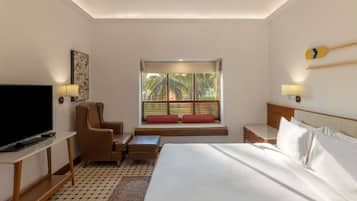 Habitación de hotel con cama, televisión, silla, mesita pequeña, ventana con persianas y ventilador de techo.
