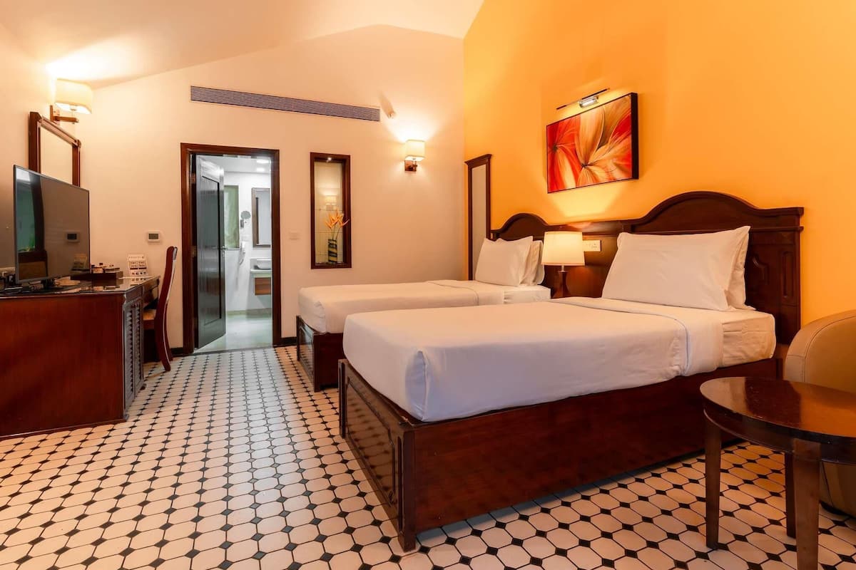 A hotel room with two beds, a desk, a TV, and a bathroom visible through an open door.