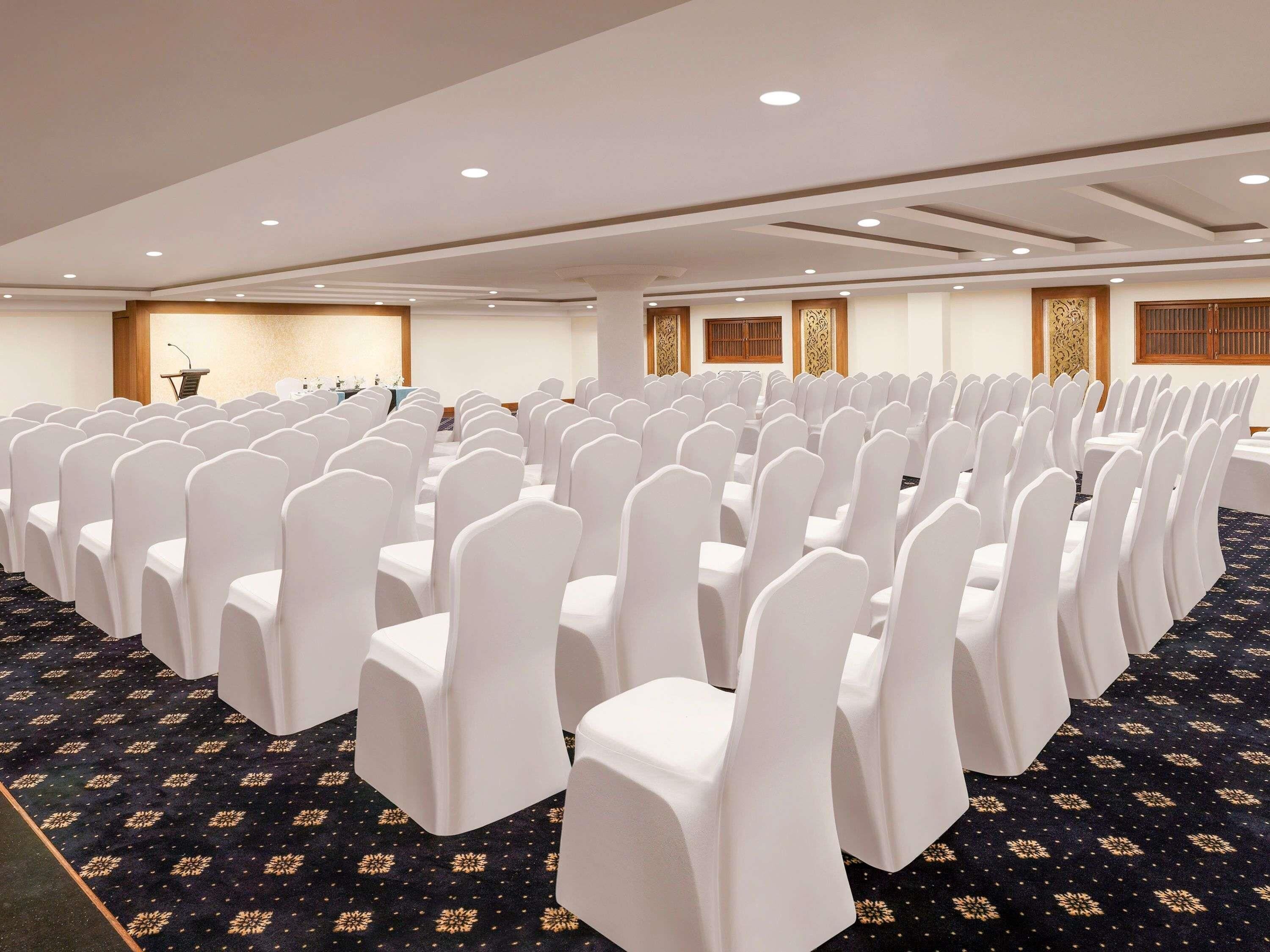 A conference room with rows of white chairs, a podium, and a carpeted floor.