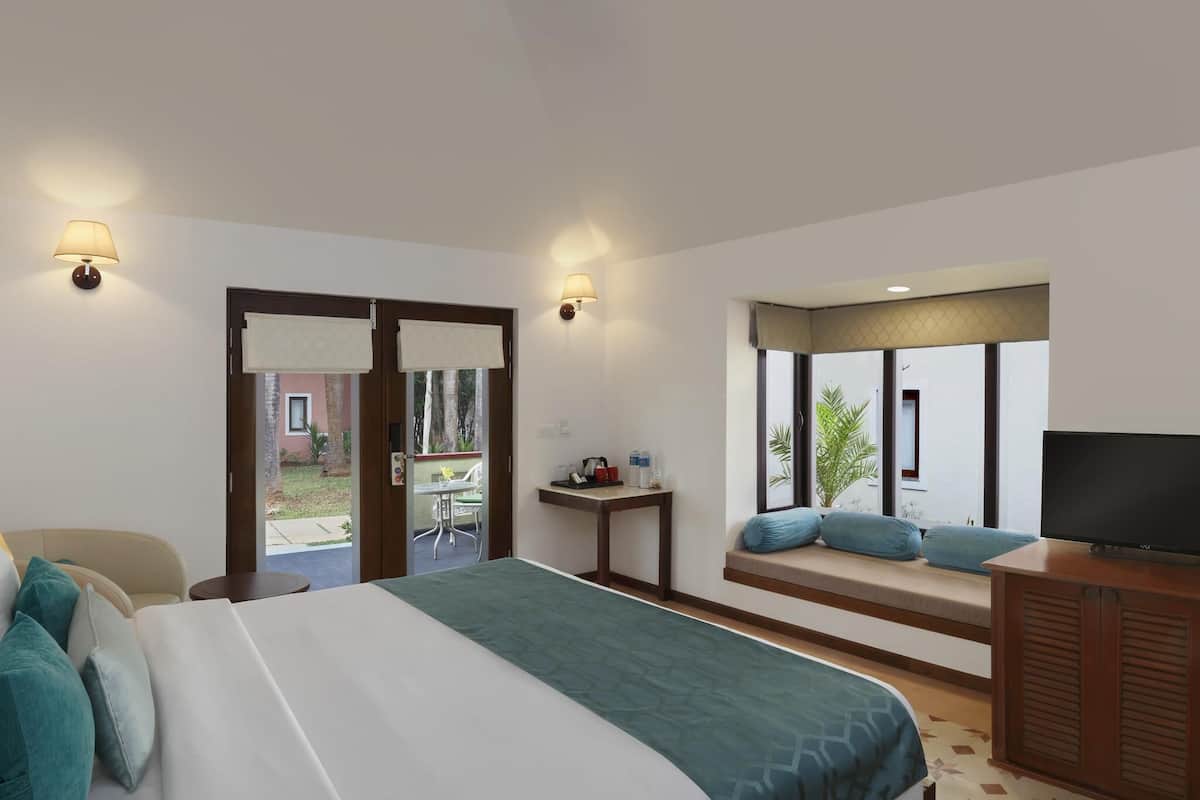 A hotel room with a bed, a TV, a small table, and a window with a view of the outside.