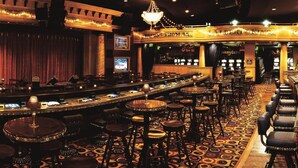 A bar area with multiple stools and tables, a stage with curtains, and a chandelier.