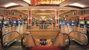 A casino floor with multiple slot machines, escalators, and a decorative chandelier.